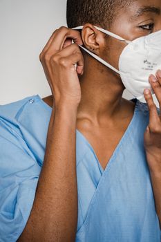 Crop African American female doctor in blue uniform adjusting protective mask and looking away