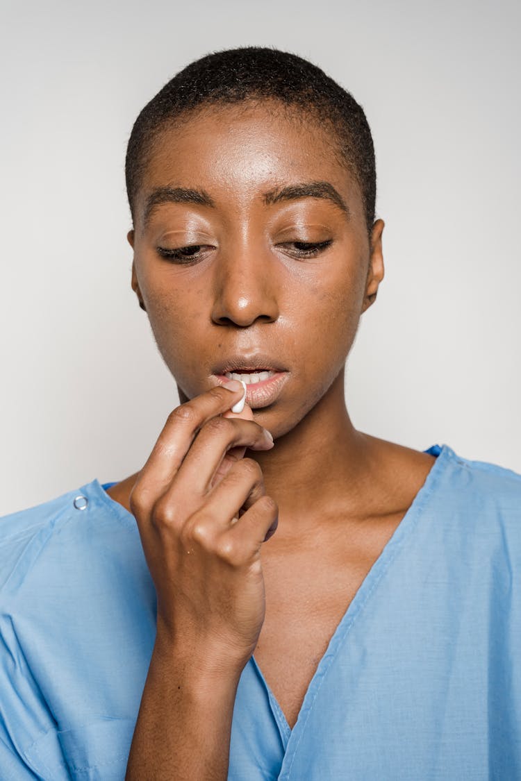 African American Female Patient Taking Pill In Studio