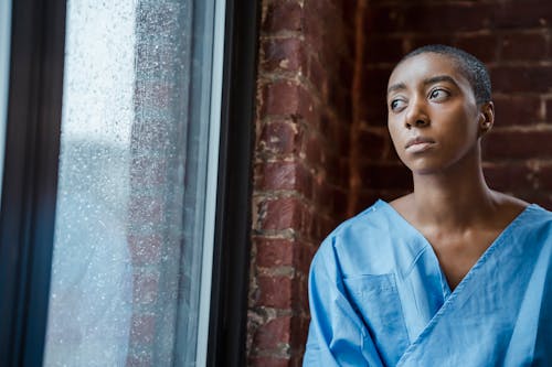 Free Thoughtful androgynous black woman looking at window in rainy day Stock Photo
