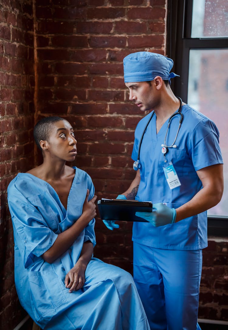 Doctor Communicating With Black Patient In Hallway Of Hospital