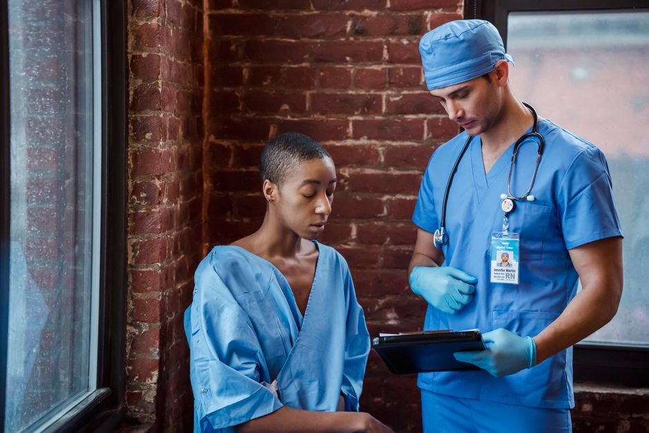 Pensive man nurse in blue uniform standing and demonstrating diagnosis to serious African American female patient in hallway of hospital in daytime