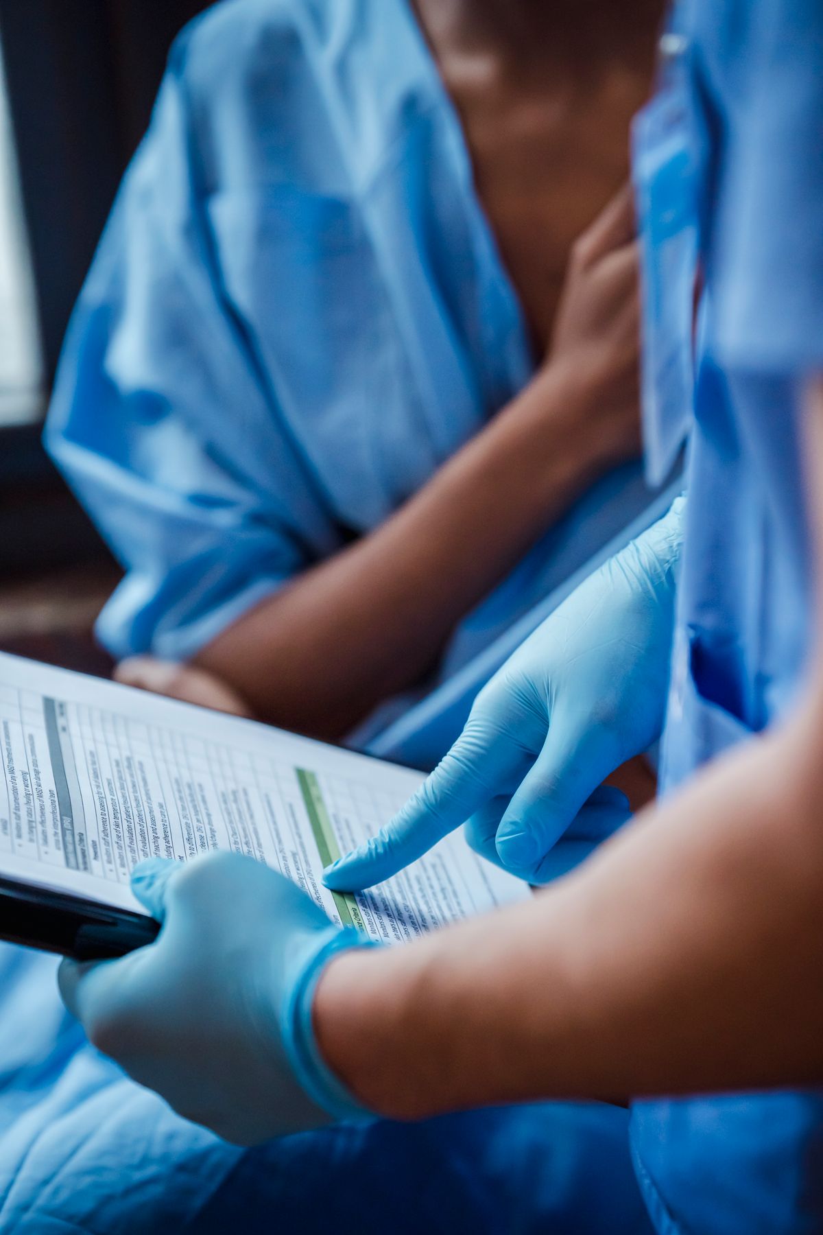 A clinician in scrubs and gloves shows a diagnosis on a clipboard to a Black woman patient during a clinic consultation after breast imaging.