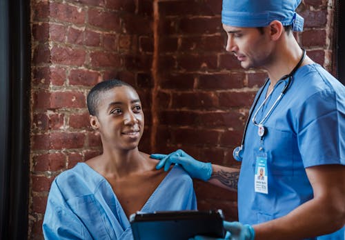 Cheerful black patient talking with doctor in hallway of hospital