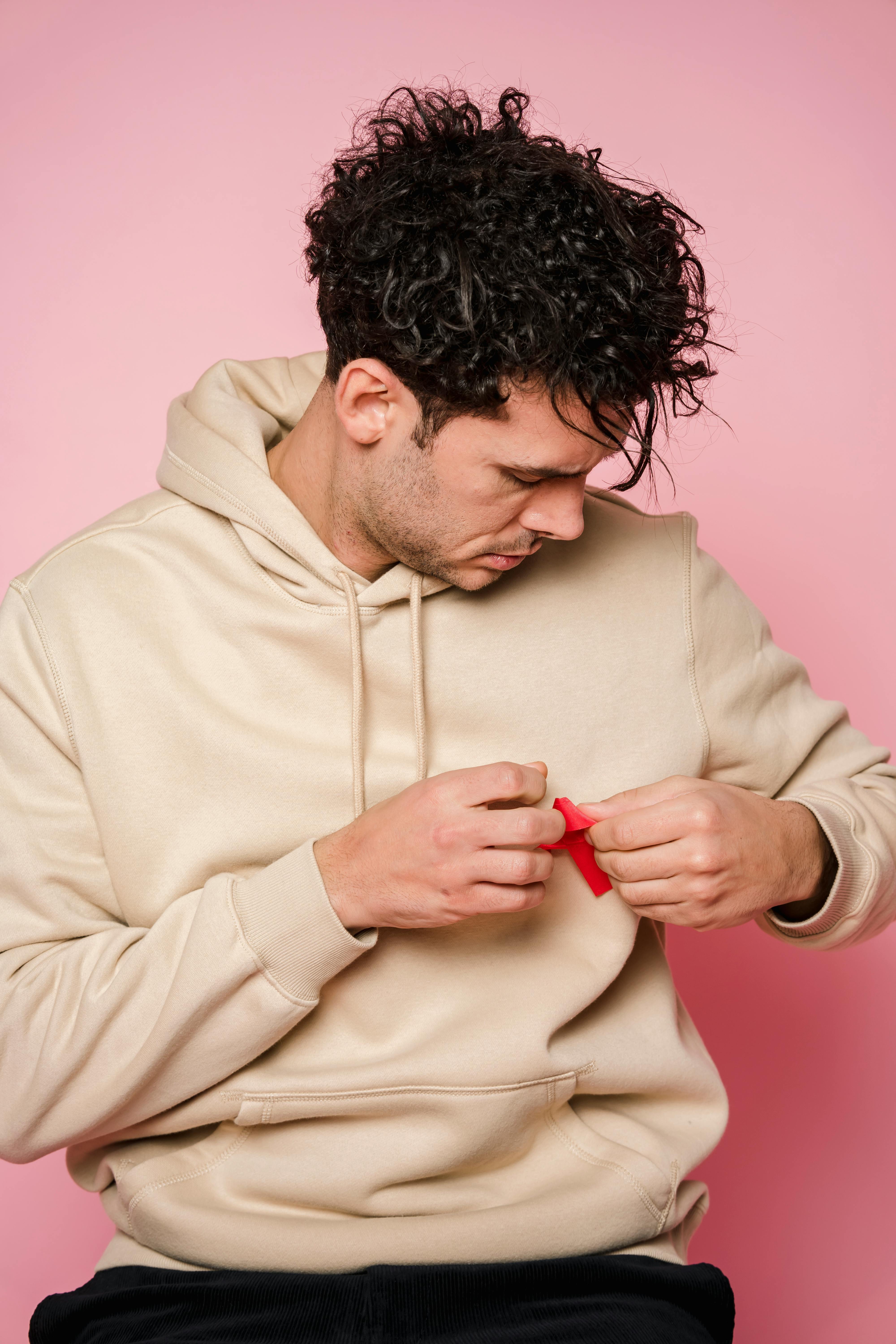 Young man attaching a red ribbon to a beige hoodie, symbolizing awareness.