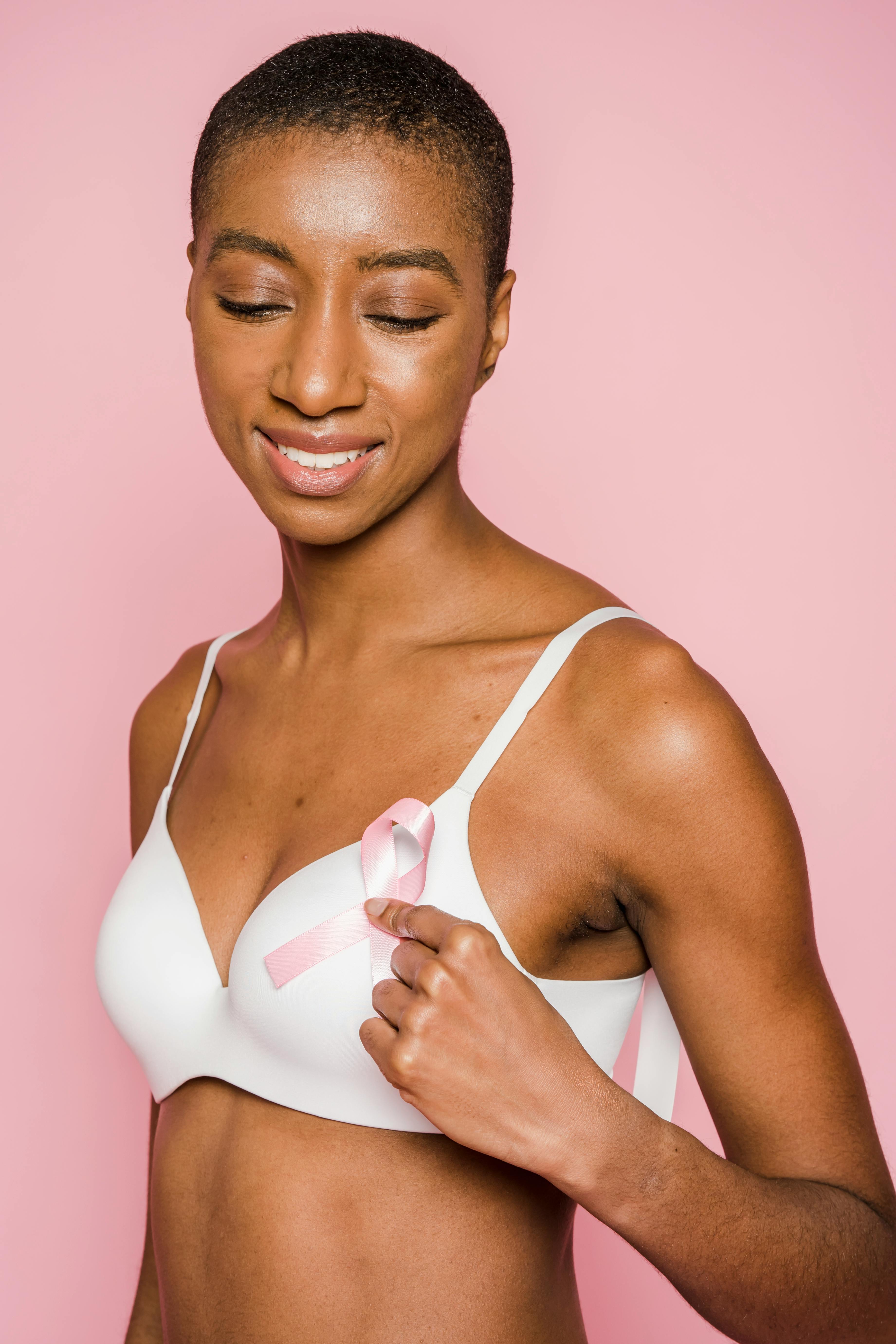 cheerful black woman in lingerie looking down against pink background