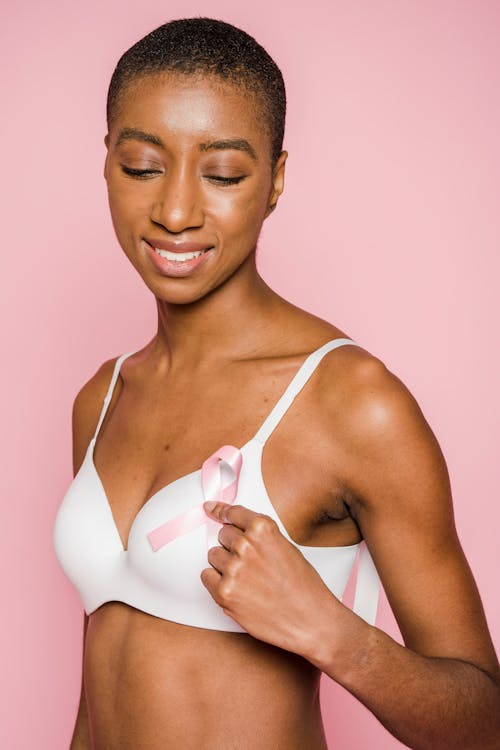 Cheerful black woman in lingerie looking down against pink background