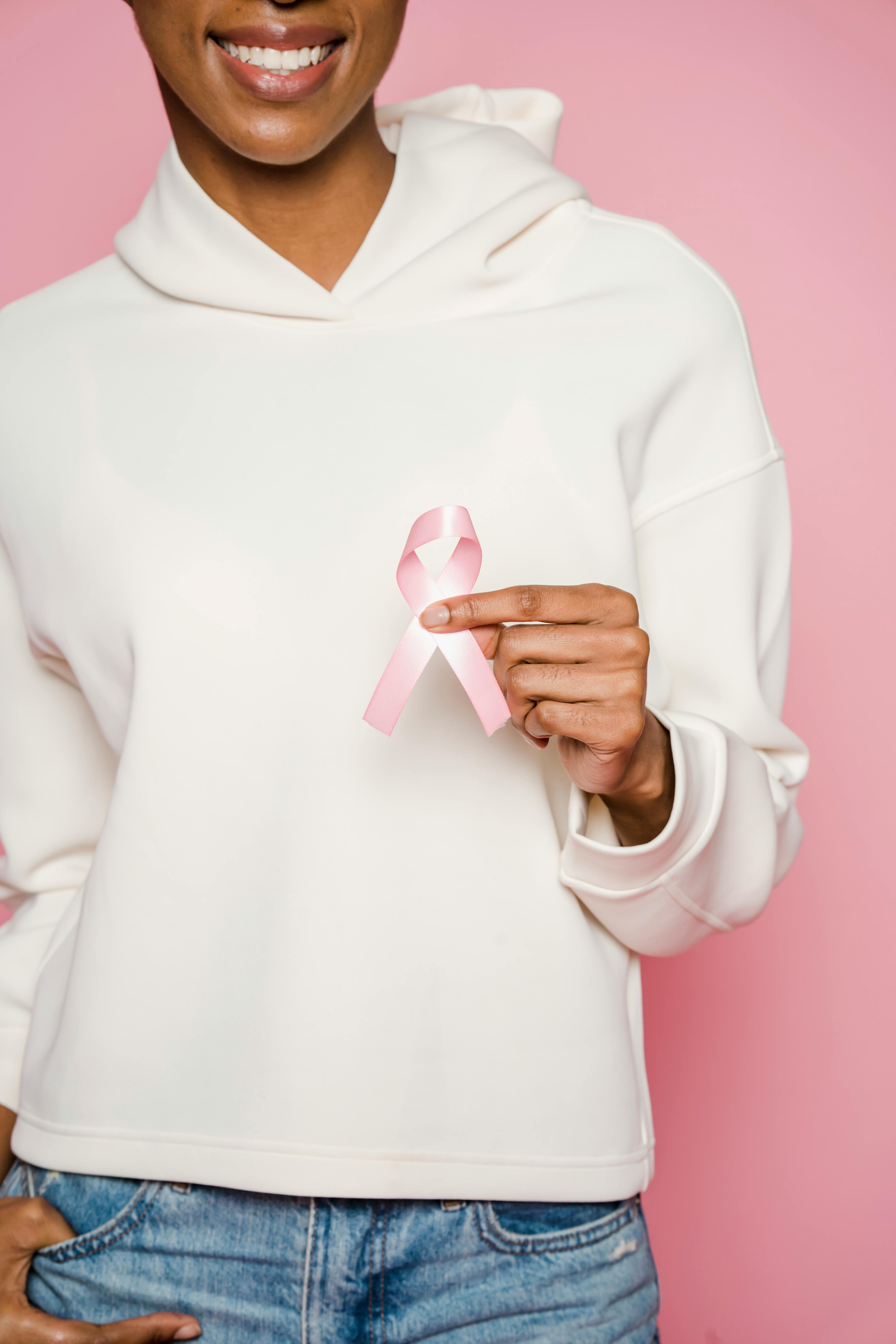 A woman in a white hoodie holding a pink ribbon symbolizing breast cancer awareness.