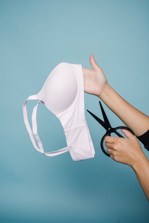 Female cutting white bra against blue wall · Free Stock Photo