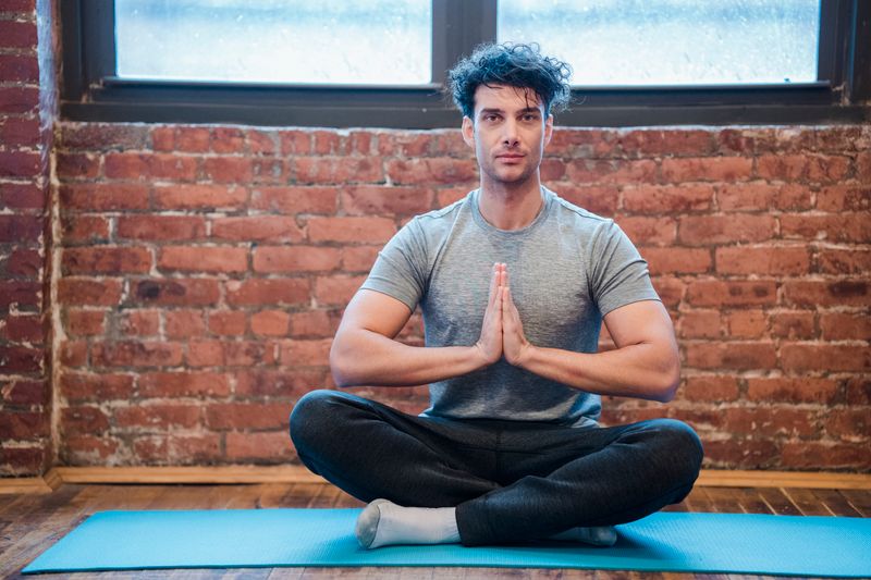 Young man sitting calmly in a meditative posture on a mat indoors