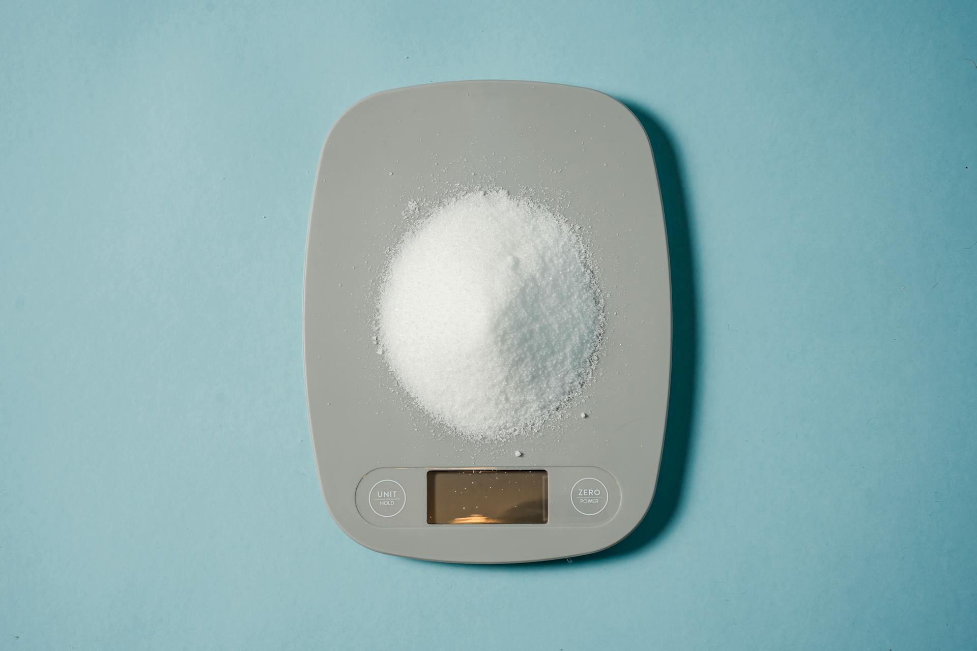 Top view of kitchen scales with electronic display measuring weight of sugar on blue background