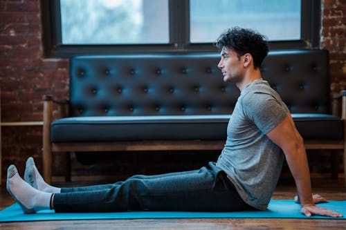 Side view full body of male sitting on sports mat while having break in training