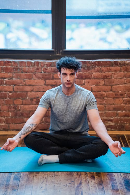 Hombre En Camiseta Gris Con Cuello Redondo Y Pantalón Negro Sentado En Estera De Yoga Azul