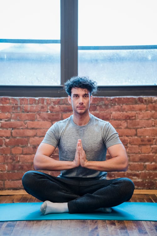 Meditating man sitting with crossed legs and namaste gesture