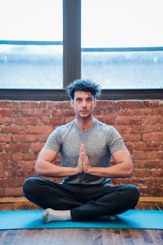 Young man meditating in a serene yoga pose on a mat indoors.