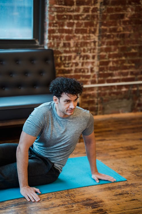 High angle of concentrated male doing twist for stretching spine while leaning on hands and looking away