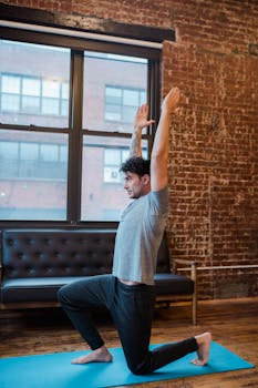 A man performs a crescent lunge yoga pose in a stylish urban loft with exposed brick walls.