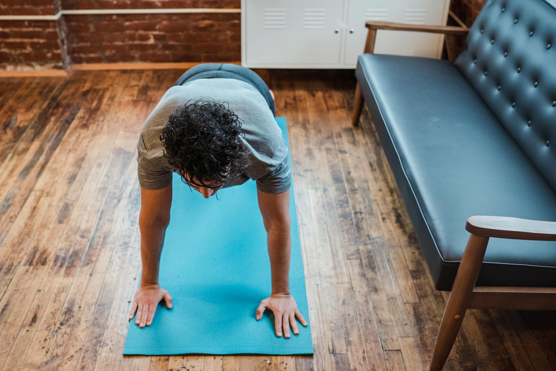 High angle of fit male doing balancing yoga posture Phalakasana for strengthening arms on sports mat near sofa