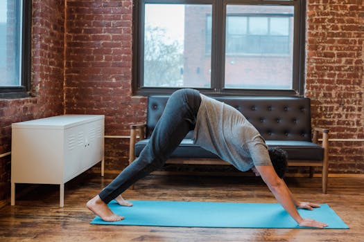 A man performs the downward dog yoga pose on a blue mat in a cozy indoor setting.