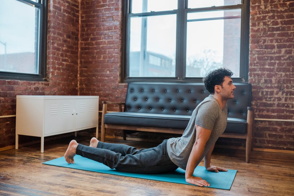 Side view full body of concentrated male lying on sports mat and stretching back muscles in Bhujangasana during yoga training