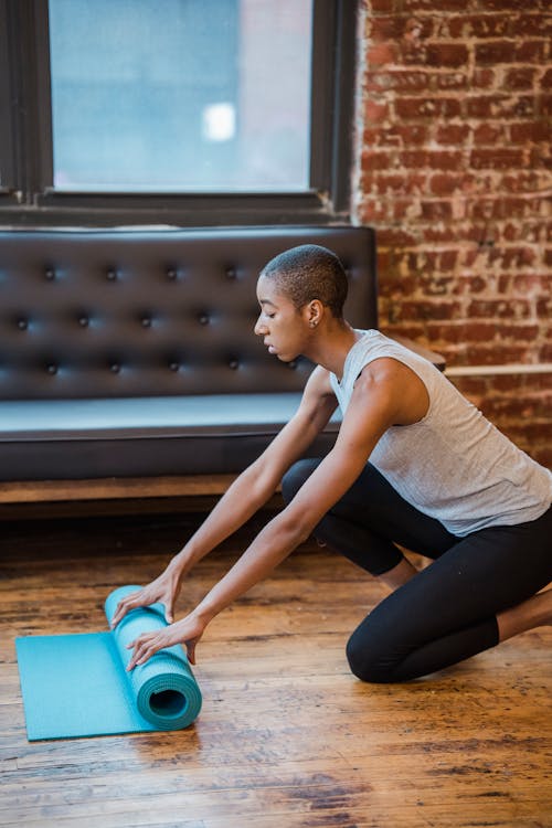 Side view of concentrated African American female in sportswear preparing mat for workout on floor