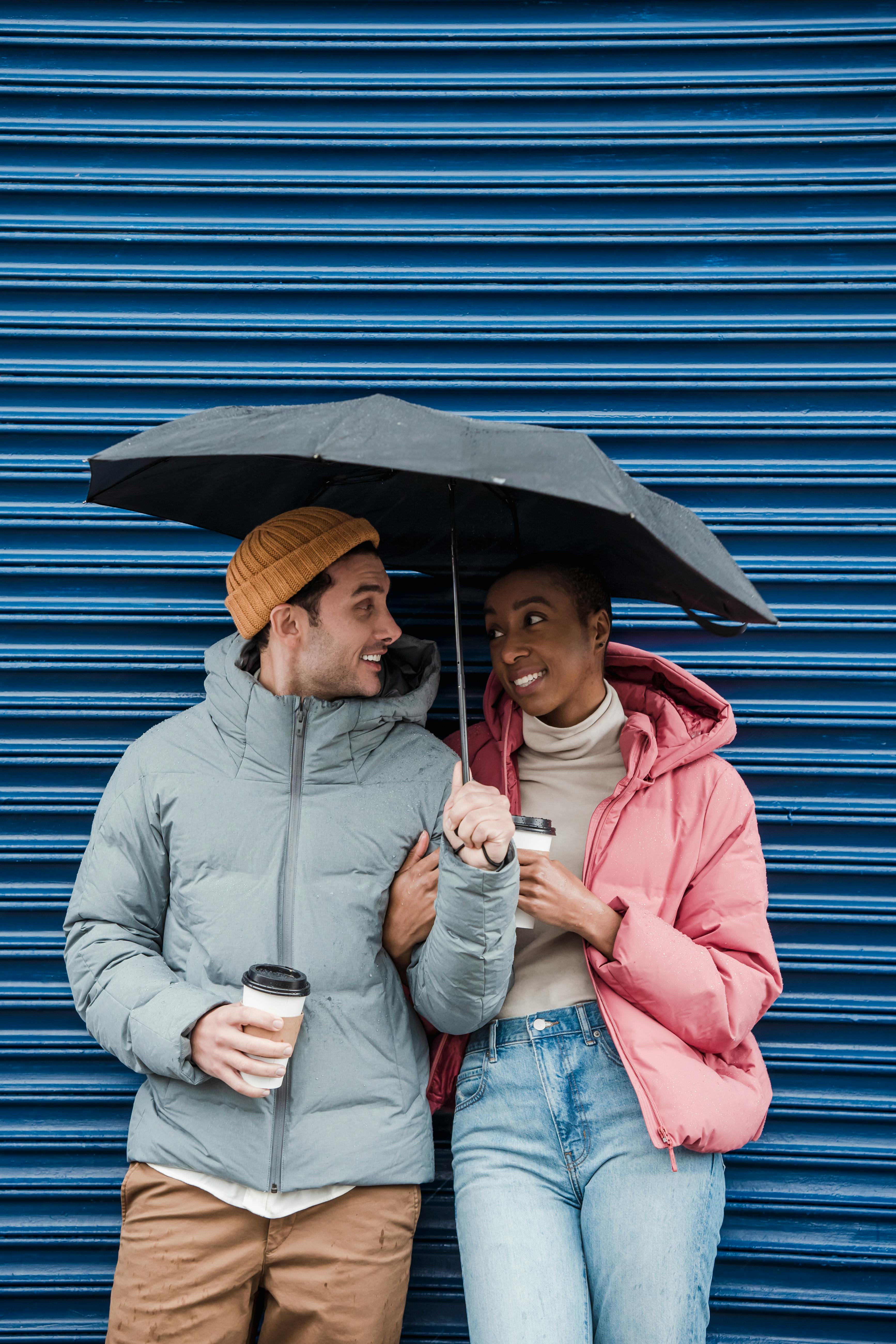 positive loving diverse couple standing under umbrella