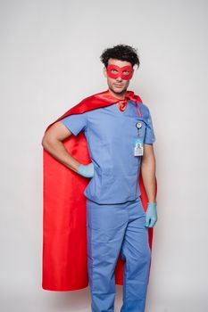 Confident doctor in medical wear and latex gloves under hero cape standing with hand on waist against gray background