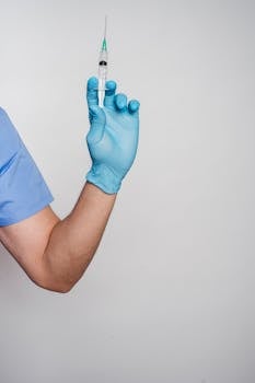 A healthcare professional's gloved hand holding a syringe for medical use.