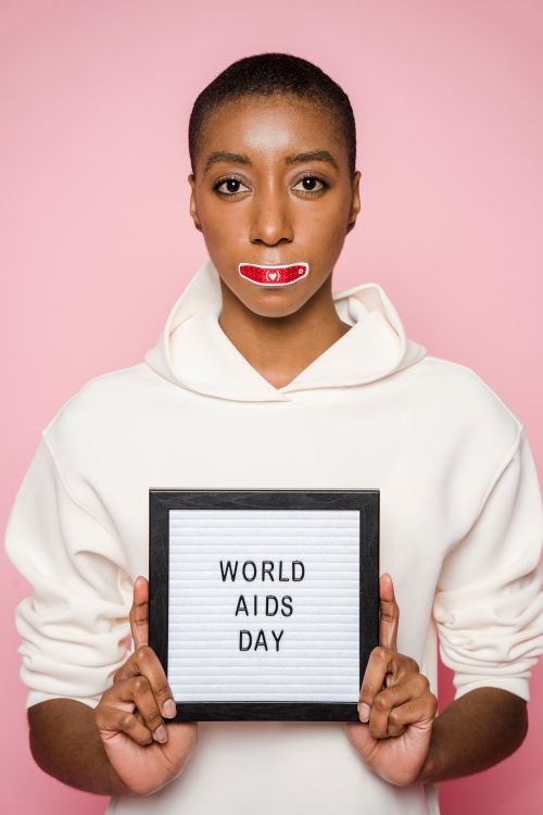 Free A woman poses with a World AIDS Day sign wearing a symbolic red ribbon. Stock Photo