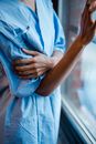 Crop anonymous ill African American female in blue patient gown near window of hospital