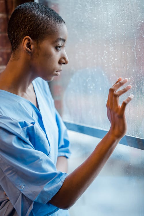 Depressed bald black woman touching wet window