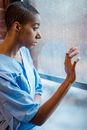 Depressed bald black woman touching wet window