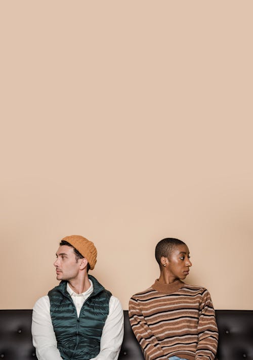 Free A diverse couple sits apart on a sofa, looking away from each other, conveying conflict. Stock Photo