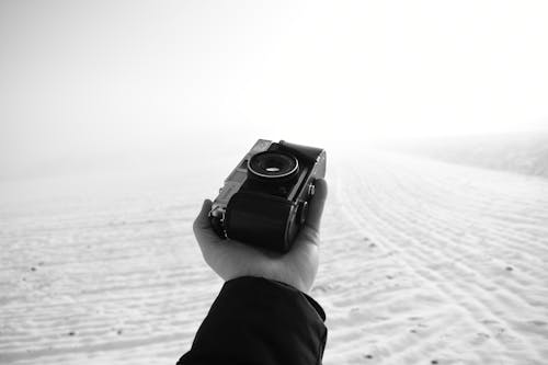 Black and white of crop anonymous male photographer with vintage photo camera in hand in snowy terrain