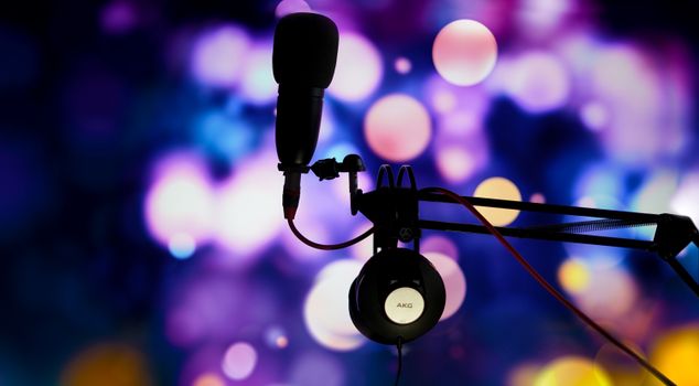 A studio microphone and headphones in silhouette against a vibrant bokeh background.
