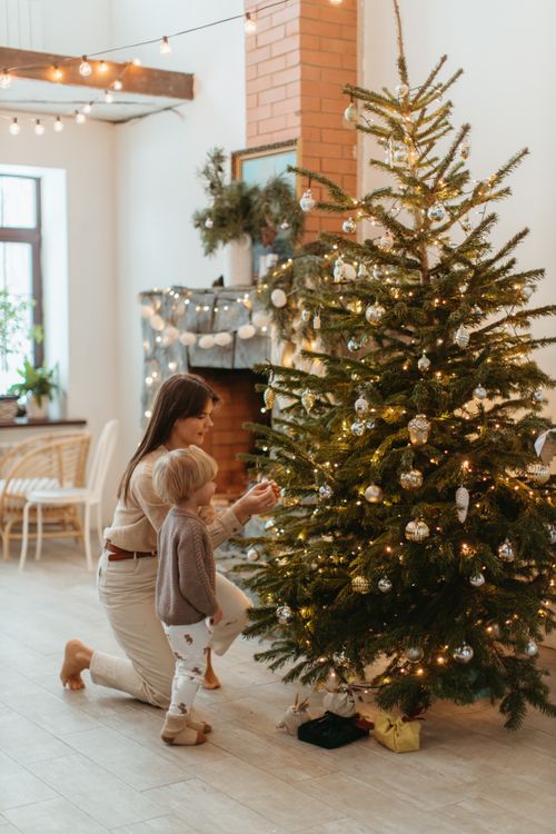 Free A heartwarming scene of a mother and child decorating a Christmas tree in a cozy home setting. Stock Photo