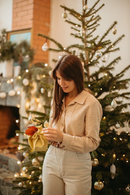 Free A Woman Holding a Present in Front of a Christmas Tree Stock Photo
