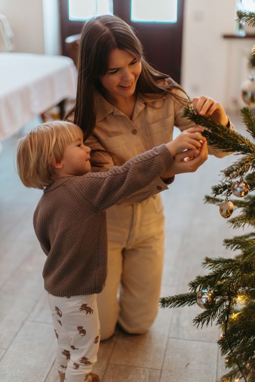 Free A joyful moment as a mother and child decorate a Christmas tree together indoors. Stock Photo