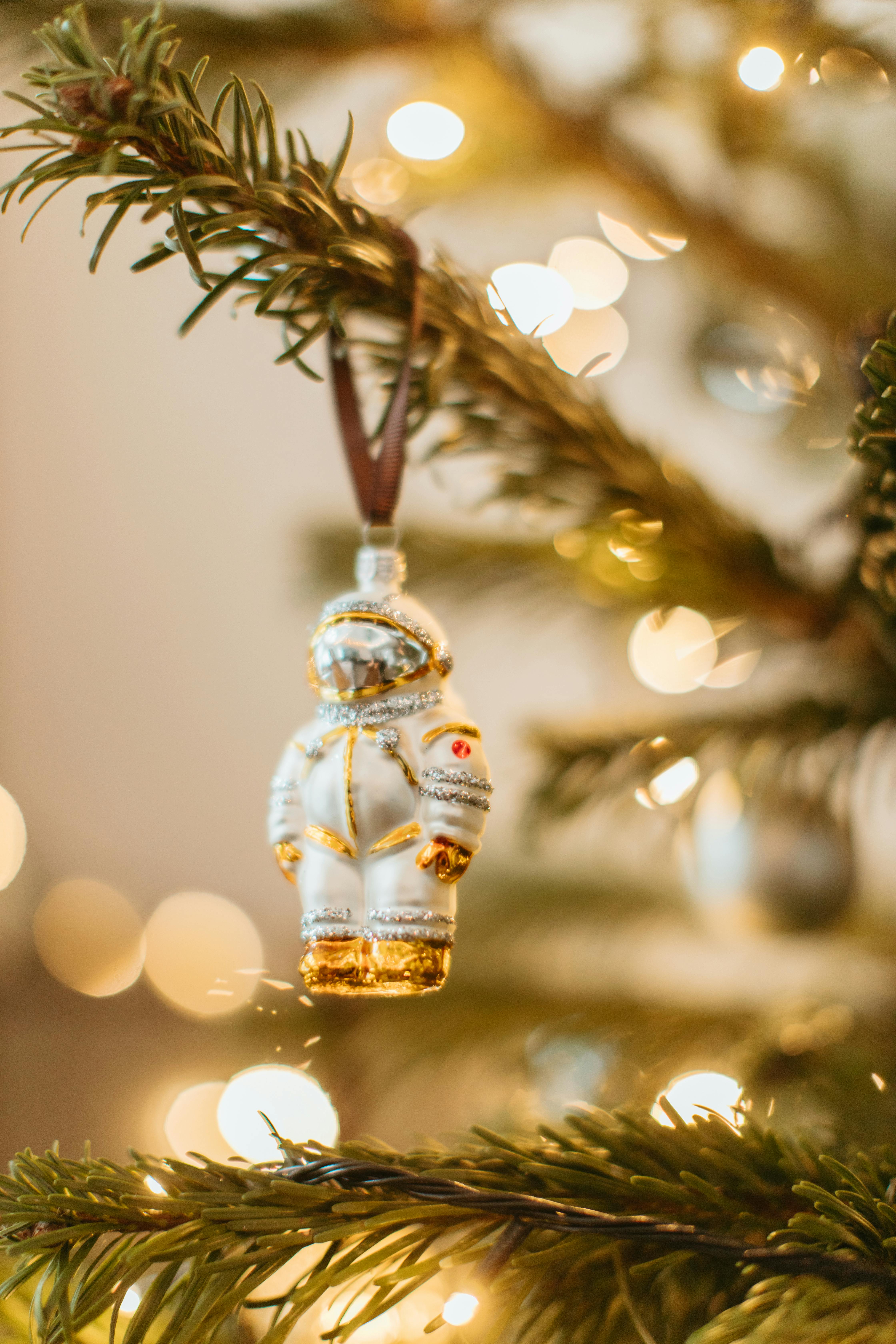 A close-up of an astronaut ornament hanging on a decorated Christmas tree with glowing lights.