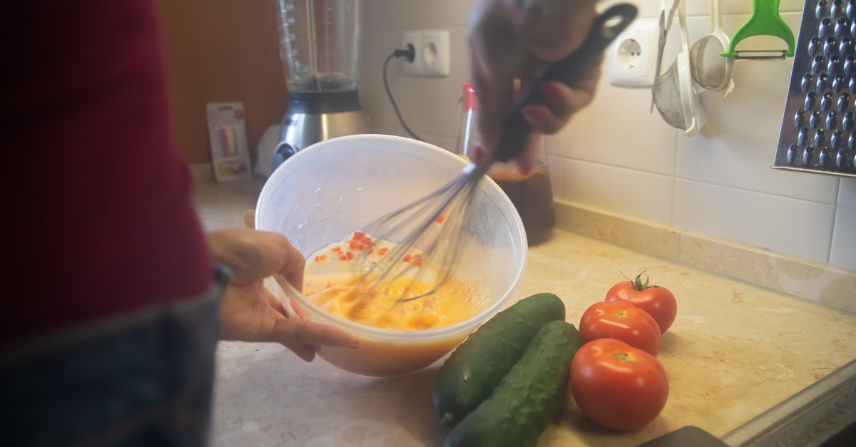Cena de cozinha com ingredientes sendo batidos e vegetais frescos.