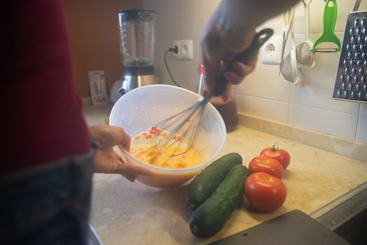 Cooking scene with whisking ingredients and fresh vegetables in a kitchen.