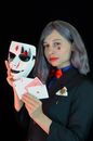 Serious young woman showing trick with playing cards in black studio