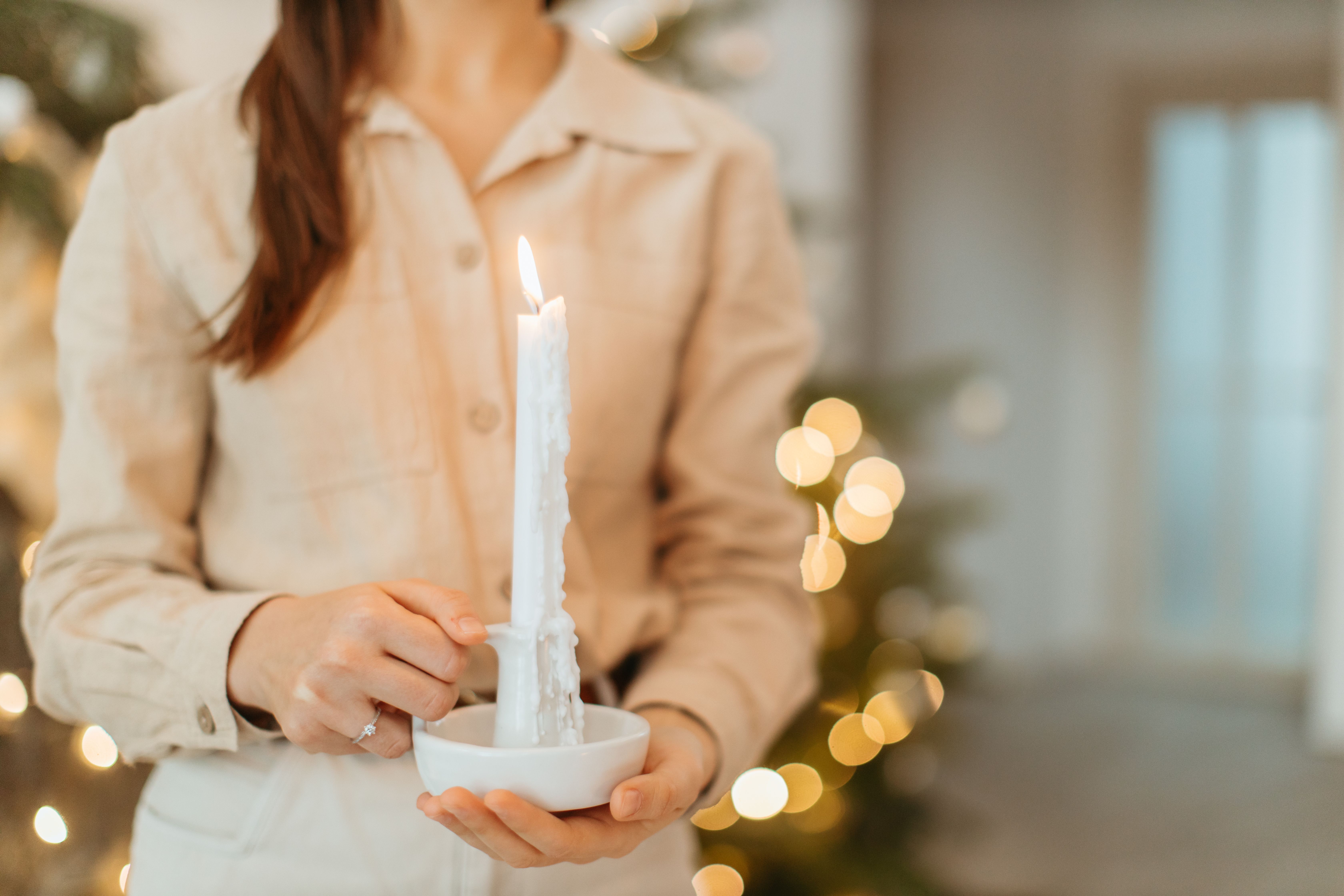 Uma imagem em close de uma mulher segurando uma vela acesa em ambiente interno, rodeada por uma atmosfera acolhedora.