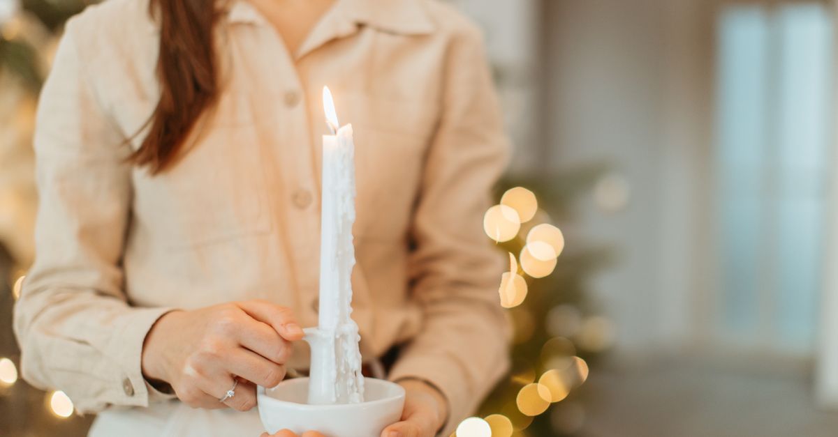 Uma imagem em close de uma mulher segurando uma vela acesa em ambiente interno, rodeada por uma atmosfera acolhedora.