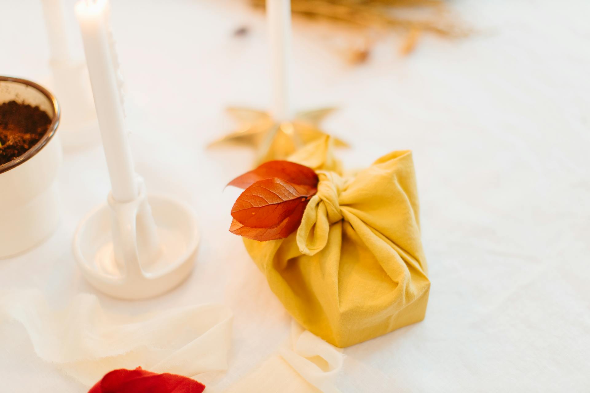 A beautifully wrapped gift with fall leaves, amidst cozy candles and natural decor.