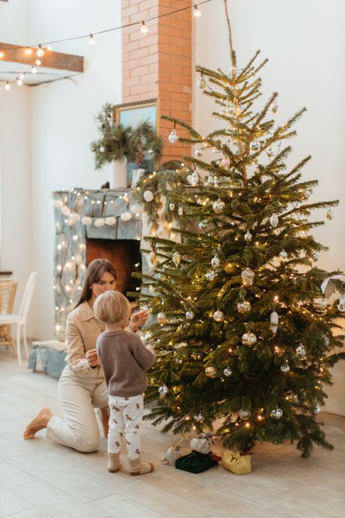 Free A festive indoor scene of a mother and child decorating a Christmas tree with ornaments. Stock Photo
