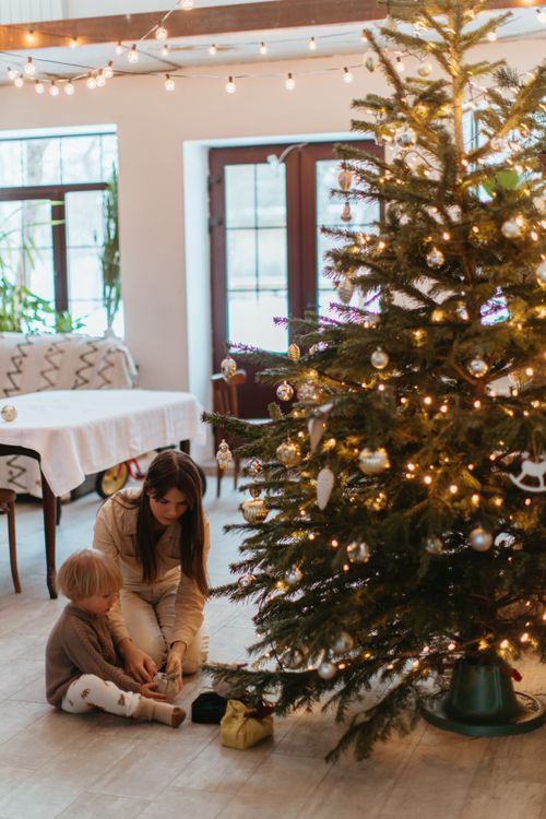Free A mother and child sitting by a decorated Christmas tree, enjoying a festive moment indoors. Stock Photo