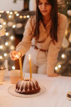 Warm holiday scene with a woman lighting candles on a cake in a festive setting.