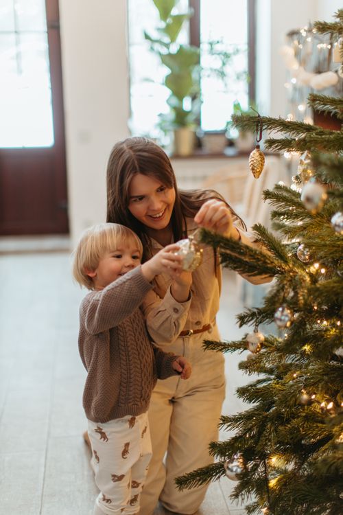 Free A mother helps her child decorate a Christmas tree in a cozy indoor setting. Stock Photo
