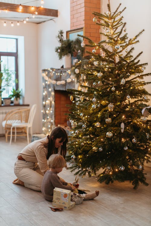 A Child Sitting next to a Christmas Tree with his Mom