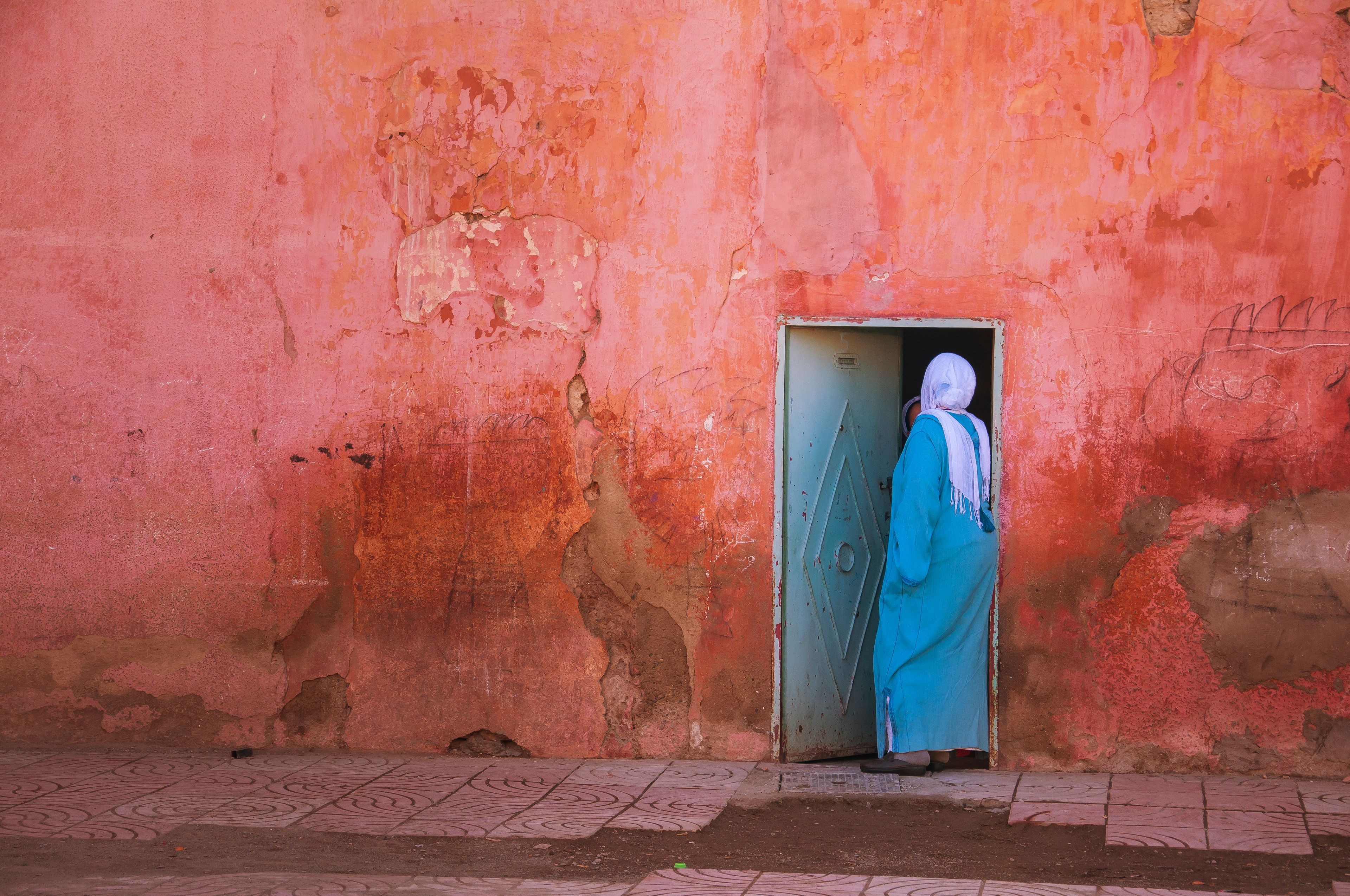 Anonymous Muslim female in traditional hijab and dress standing in doorway on shabby typical residential house in Marrakesh